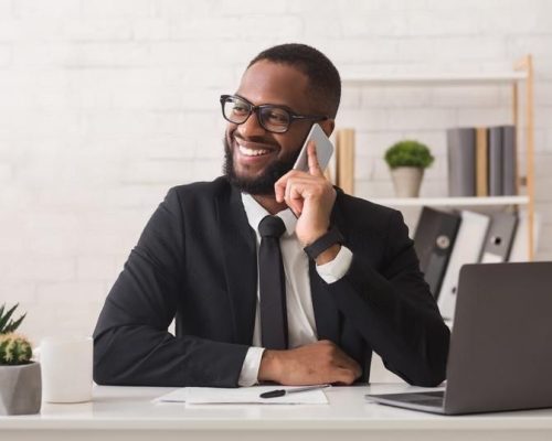 heureux-entrepreneur-noir-ayant-une-conversation-agreable-avec-ses-collegues-par-telephone-dans-les-lunettes-a-l-interieur-165580487-transformed